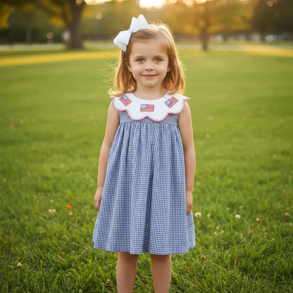 Young girl in a blue checkered dress with American flag details standing in a grassy field.