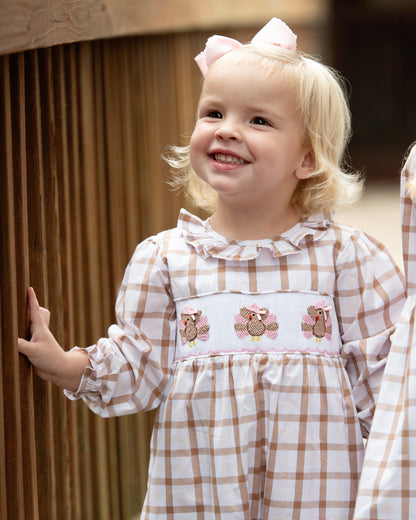 Young girl in a checkered dress with turkeys designs, standing indoors.
