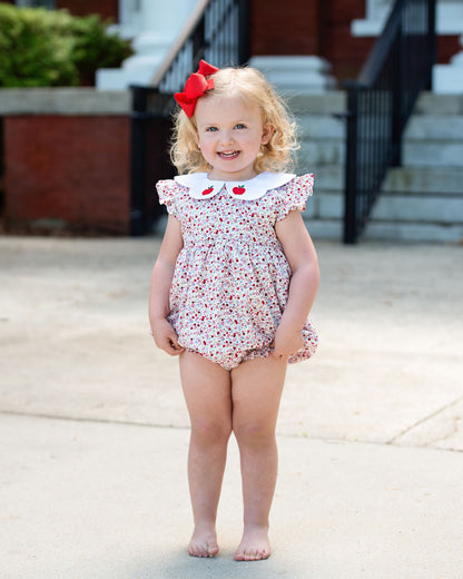 Young girl in a floral bubble with a red bow standing outdoors.