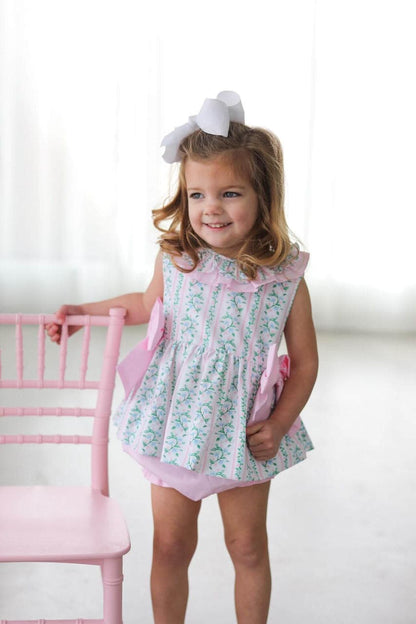 Young girl in a floral diaper set with pink trim standing next to a pink chair.
