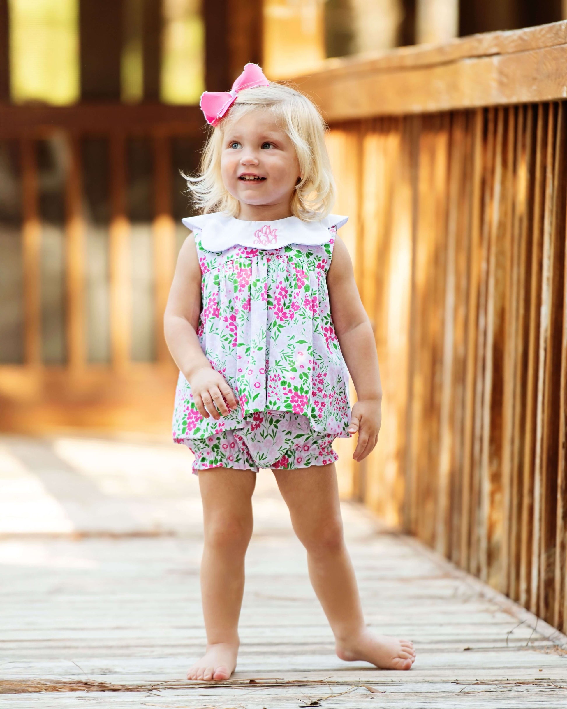Young girl in a floral dress and shorts standing on a wooden deck.