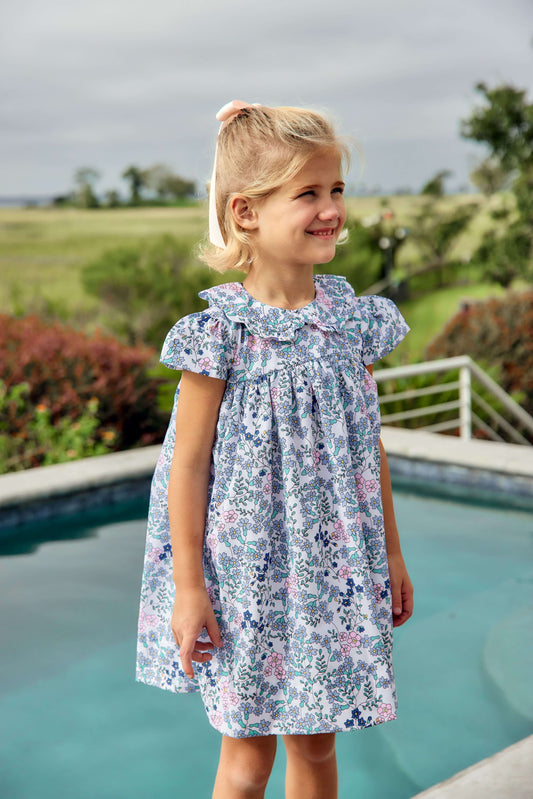 Young girl in a floral dress standing by a pool with a scenic background