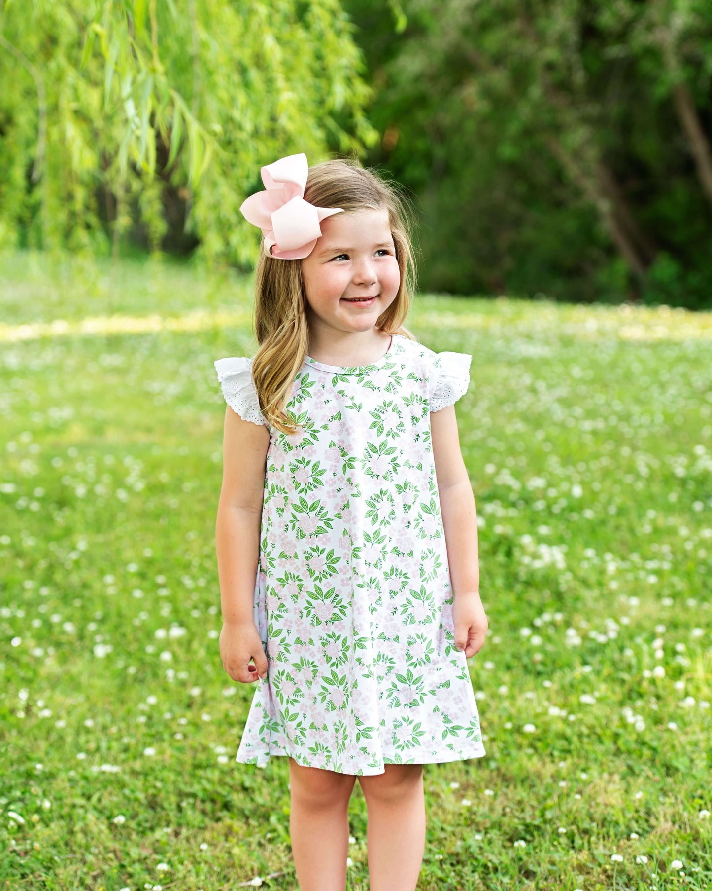 Young girl in a floral dress standing in a grassy field with trees in the background