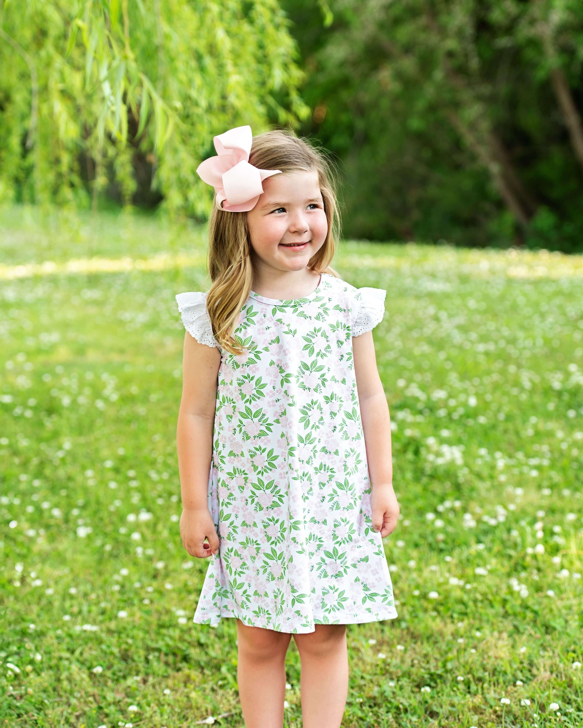 Young girl in a floral dress standing in a grassy field with trees in the background