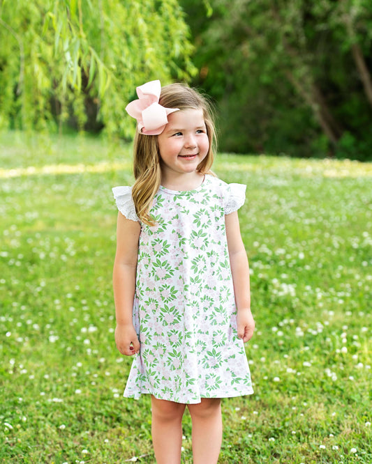 Young girl in a floral dress standing in a grassy field with trees in the background