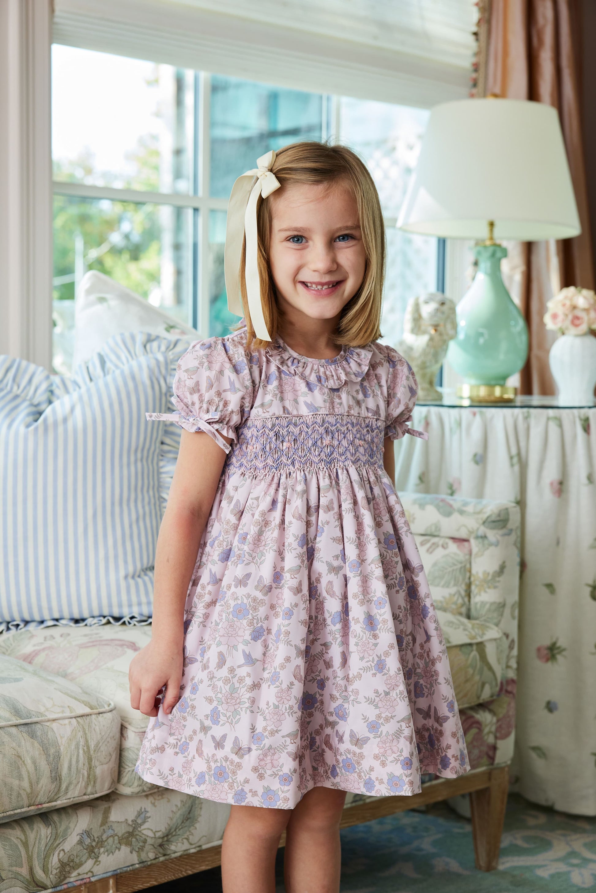Young girl in a floral dress standing in a living room.