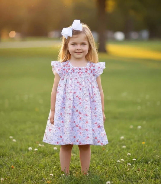 Young girl in a floral dress standing on grass with a blurred background