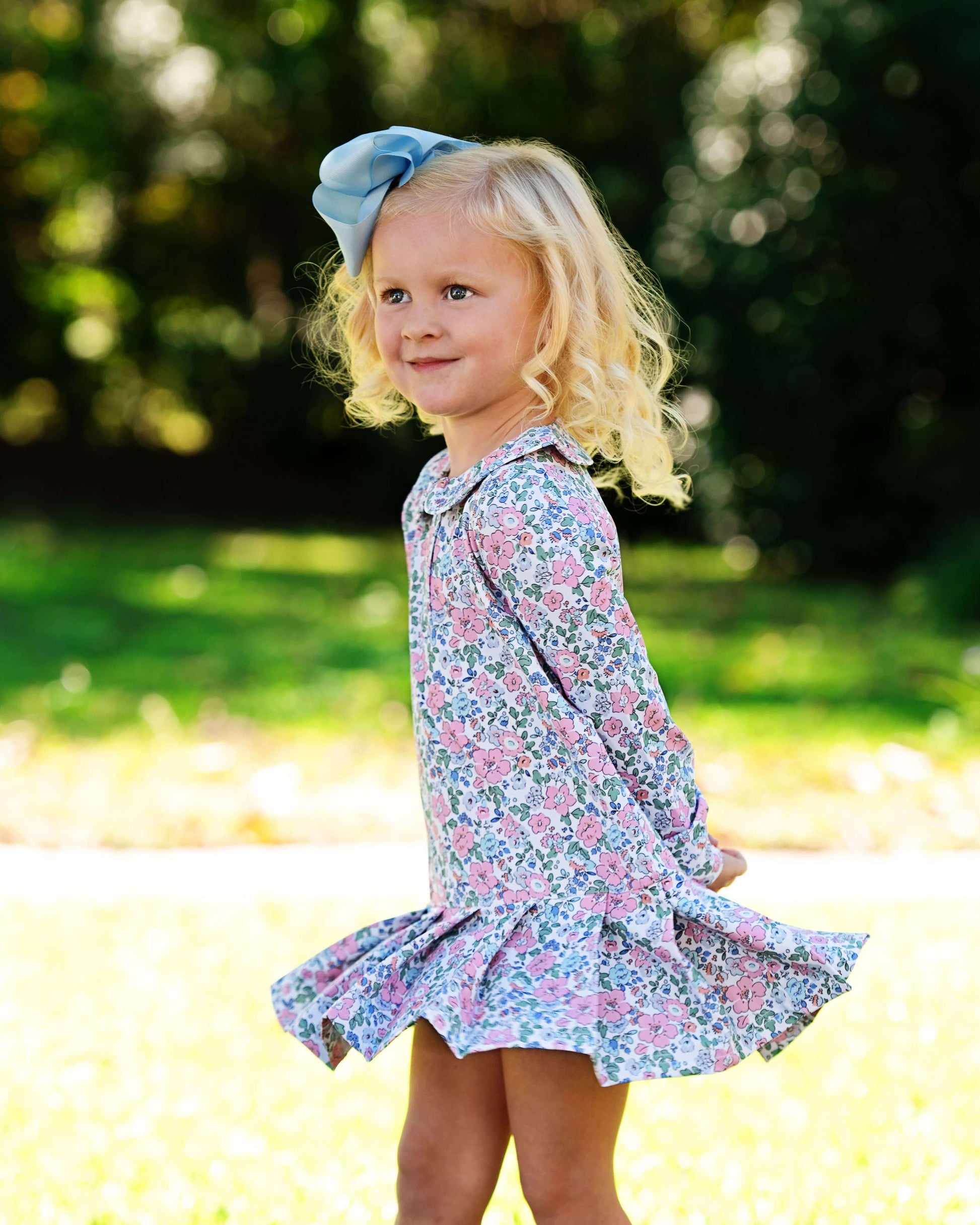 Young girl in a floral dress with a blue bow outdoors