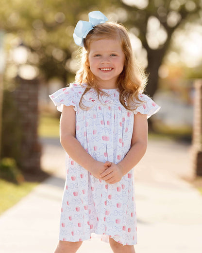 Young girl in a floral dress with a blue bow standing outdoors.