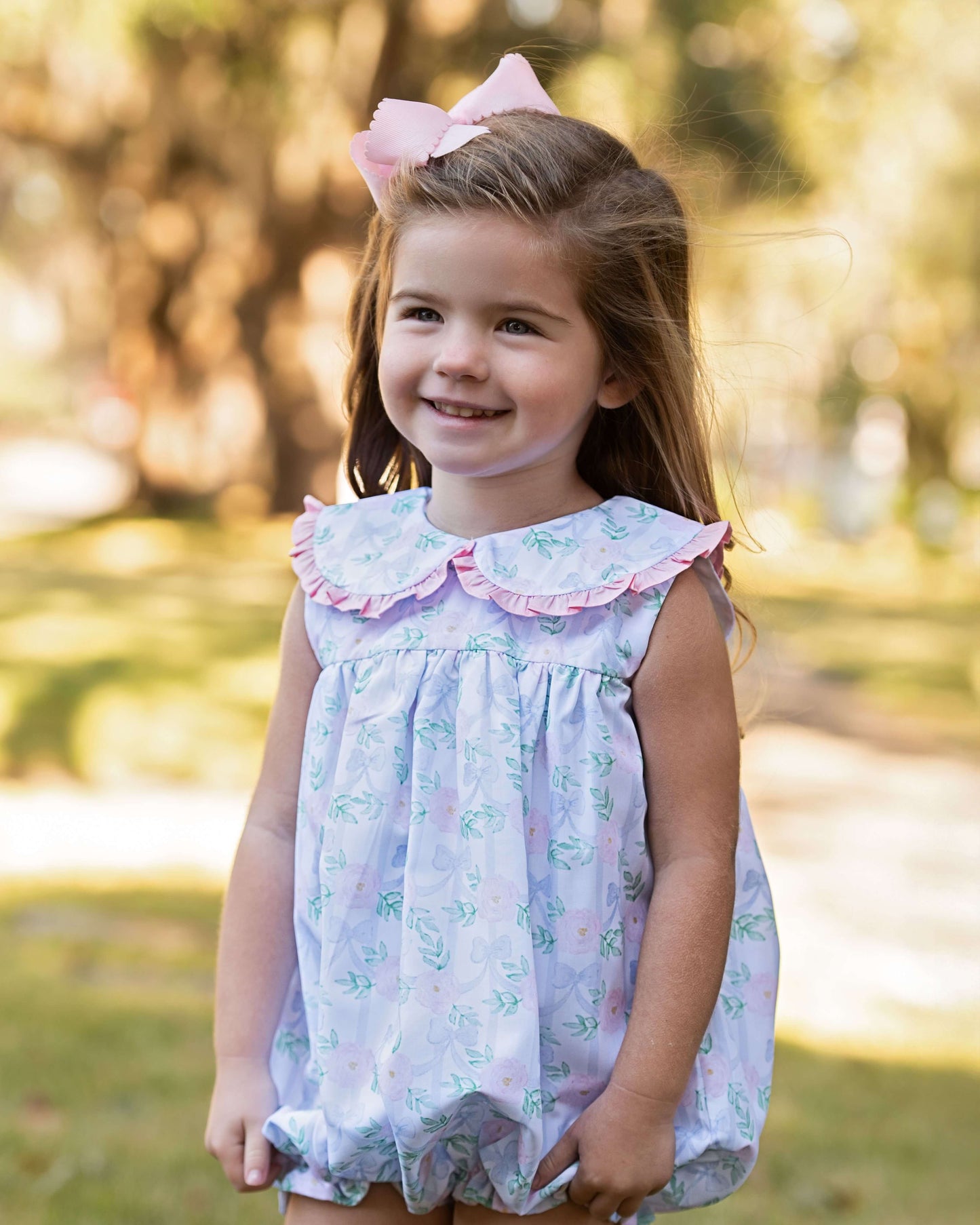 Young girl in a floral dress with a pink bow in a park setting