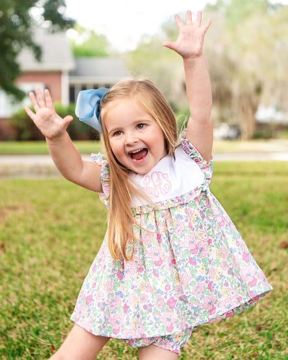 Young girl in a floral dress with arms raised outdoors