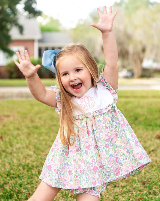 Young girl in a floral dress with arms raised outdoors