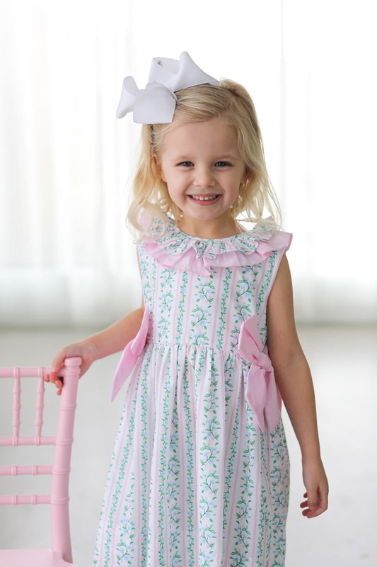 Young girl in a floral dress with pink accents standing next to a pink chair.