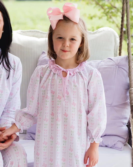 Young girl in a floral nightgown with a pink bow, sitting on a swing with a blurred background.