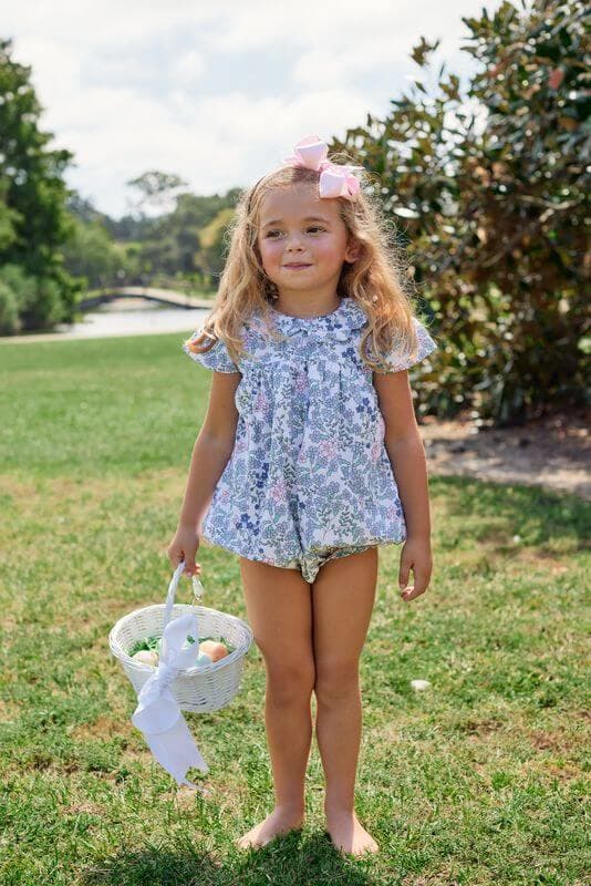 Young girl in a floral outfit holding an Easter basket outdoors.