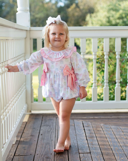 Young girl in a floral outfit standing on a wooden deck with white railings.