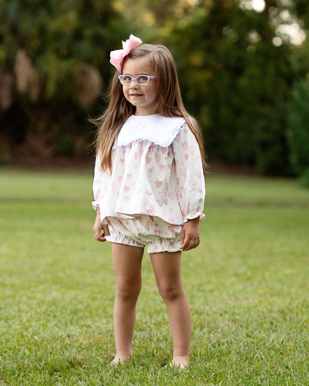 Young girl in a floral outfit standing on grass with a blurred natural background