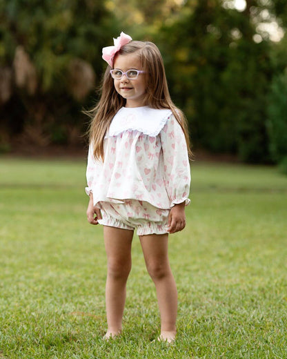 Young girl in a floral outfit standing on grass with a blurred natural background