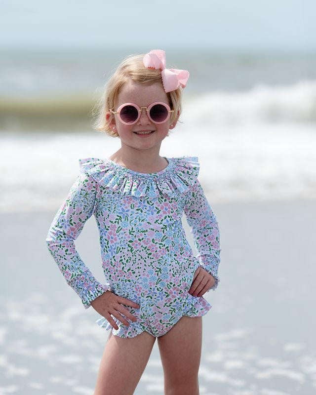 Young girl in a floral swimsuit and pink sunglasses on a beach