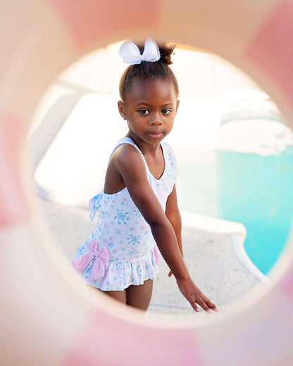 Young girl in a floral swimsuit sitting by a pool with a blurred background