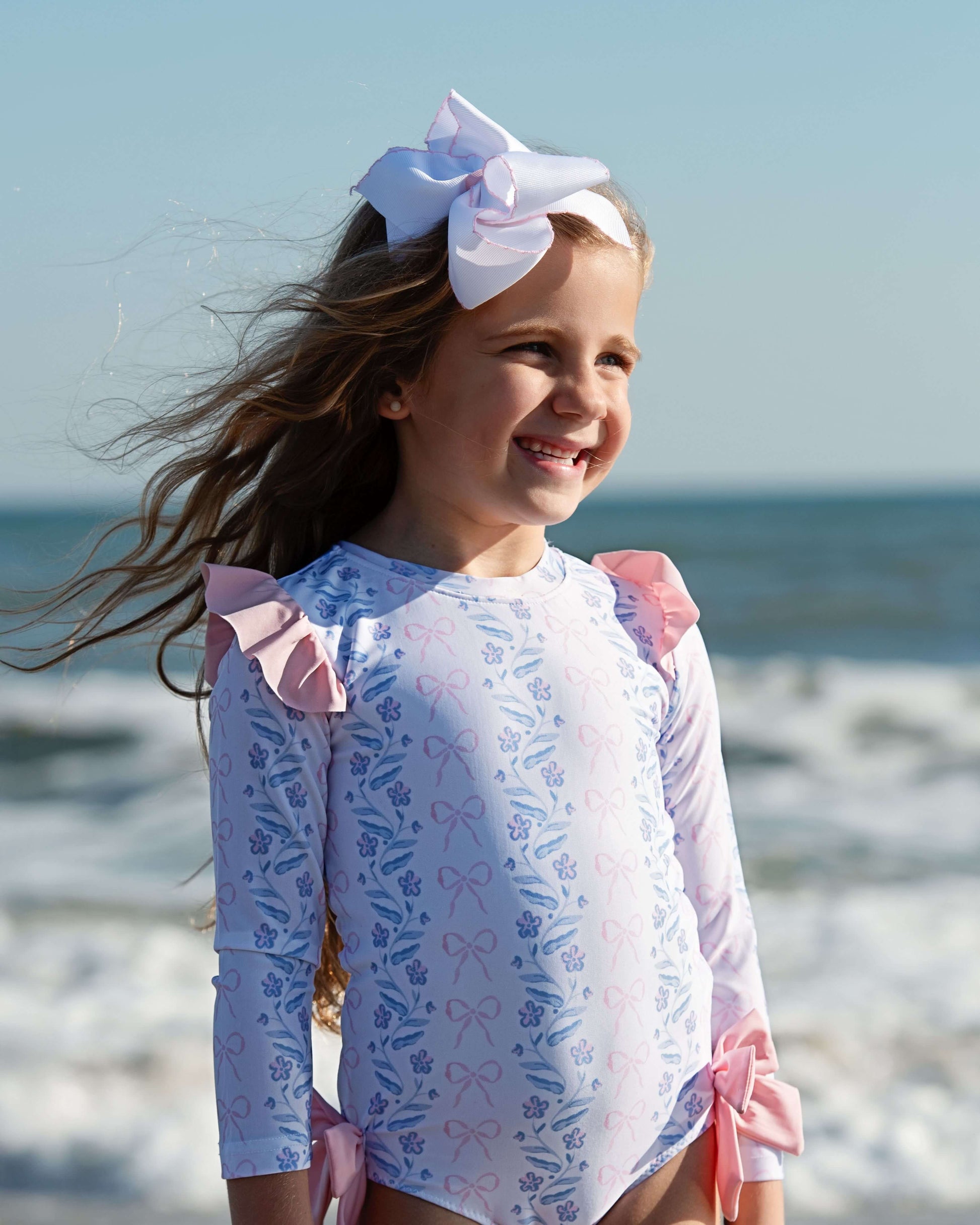 Young girl in a floral swimsuit with pink ruffles on a beach