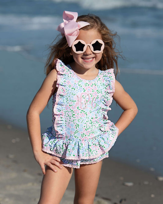 Young girl in a floral swimsuit with sunglasses and a bow on a beach
