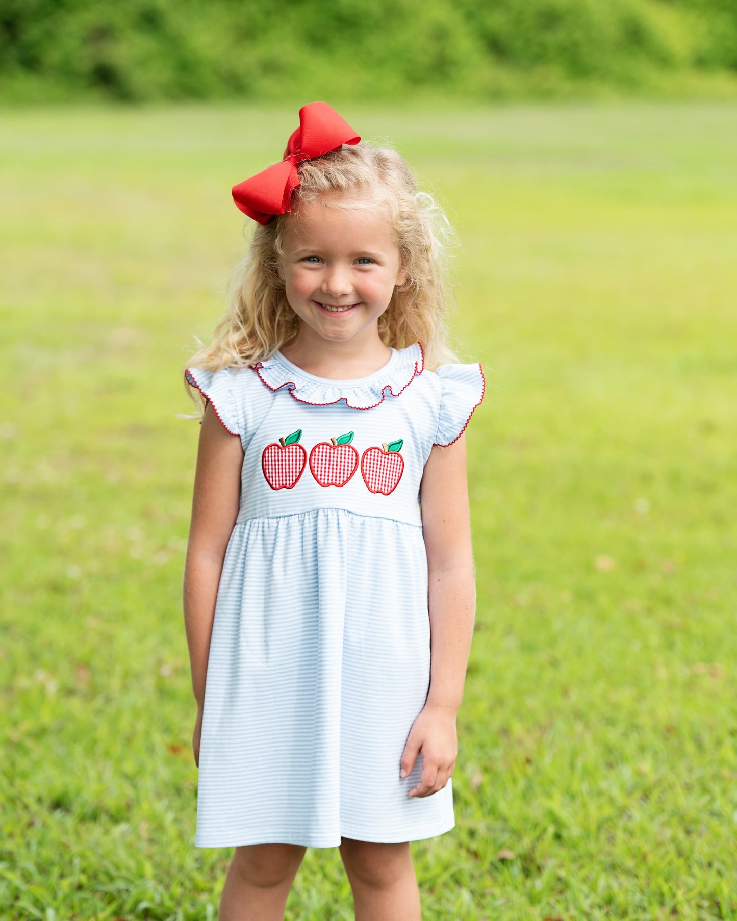 Young girl in a grassy field wearing a blue dress with apples. 