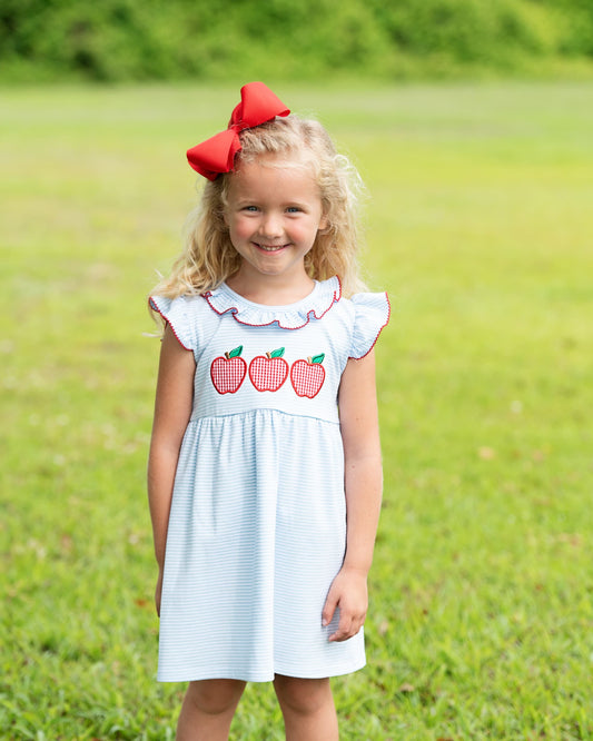 Young girl in a grassy field wearing a blue dress with apples. 
