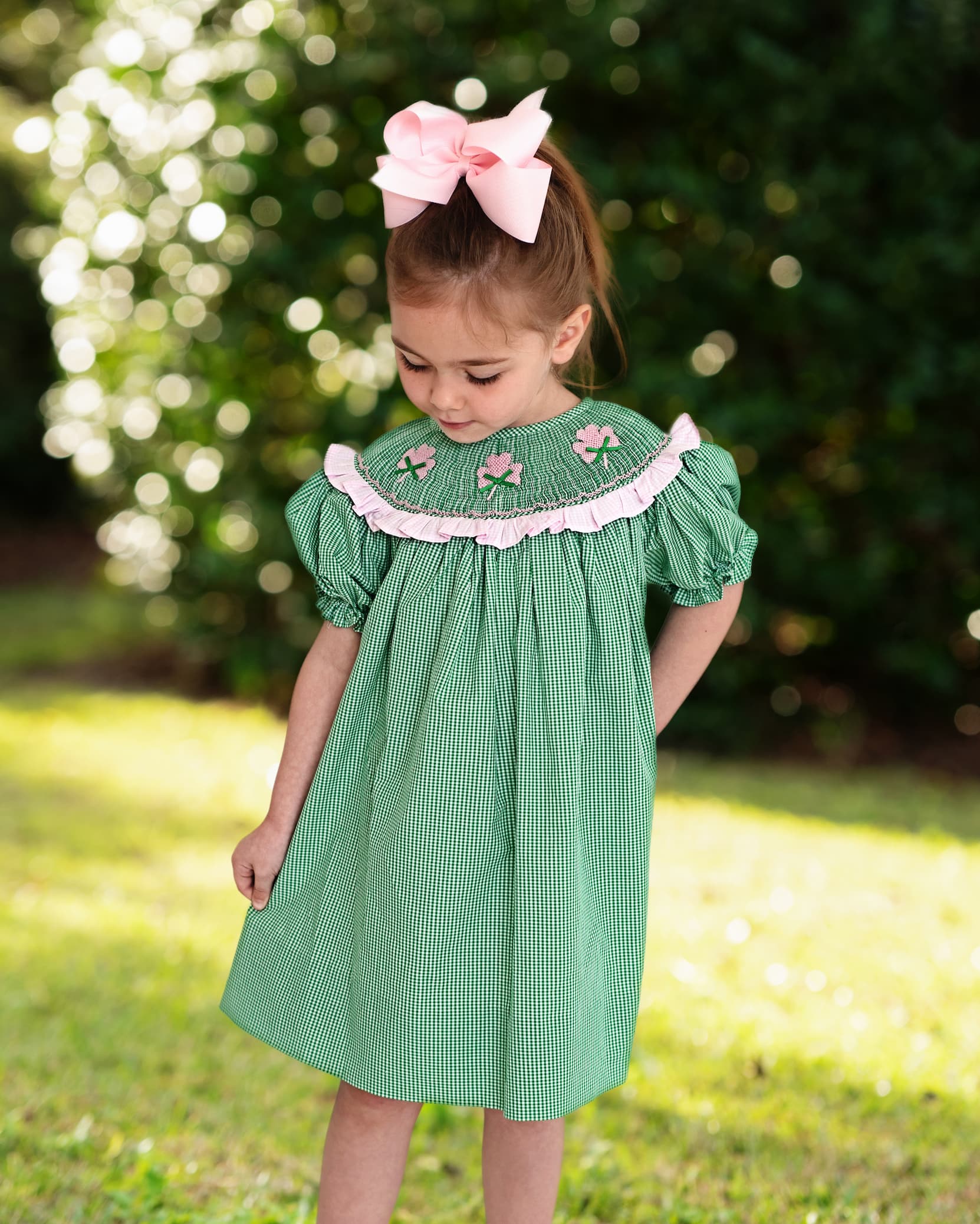 Young girl in a green dress with floral details standing outdoors with a blurred natural background