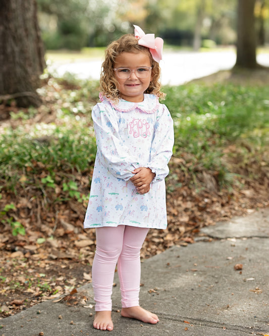 Young girl in a light-colored legging set with floral patterns and pink leggings standing outdoors.