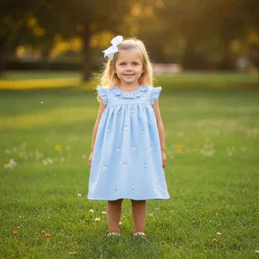 Young girl in a light blue dress with a bow standing in a grassy field.