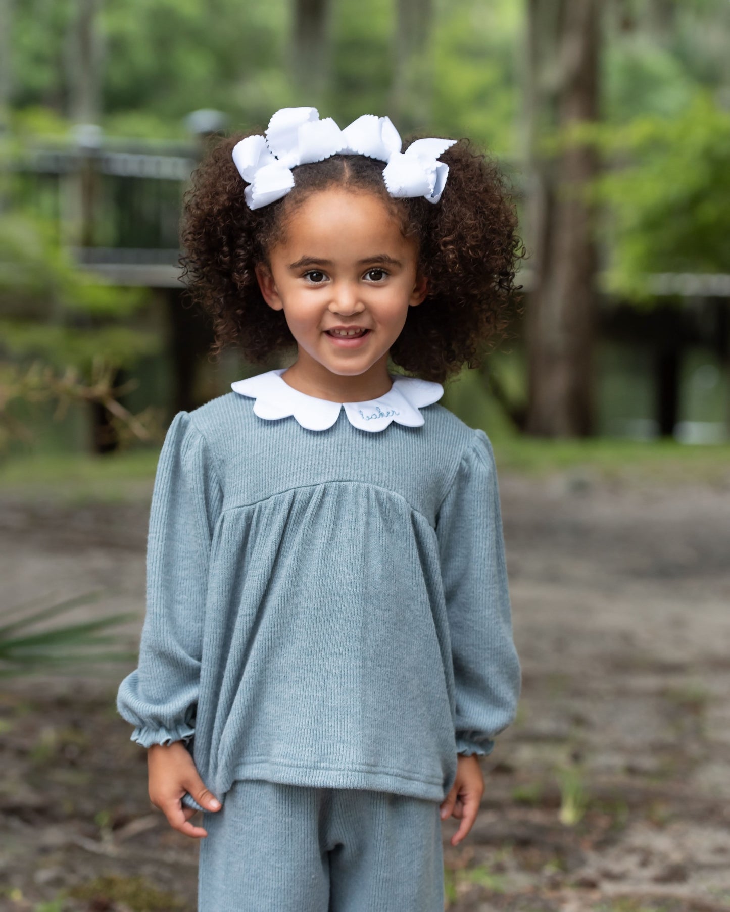 Young girl in a light blue outfit with a white collar standing outdoors.