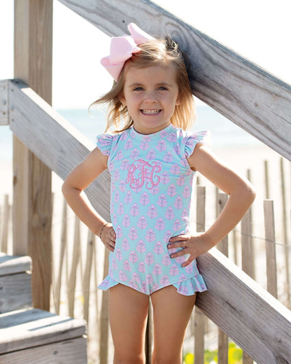 Young girl in a light blue swimsuit with pink seahorse pattern standing on a wooden deck.
