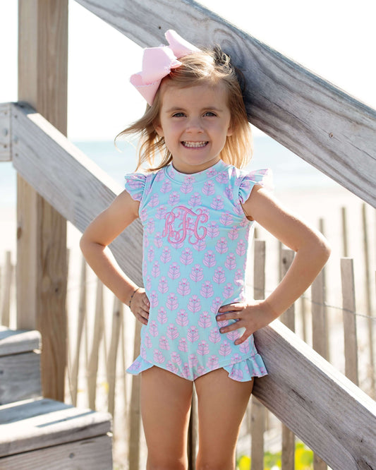 Young girl in a light blue swimsuit with pink seahorse pattern standing on a wooden deck.