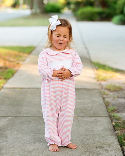 Young girl in a pink and white striped outfit standing on a sidewalk.