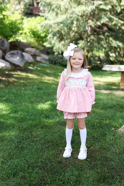 Young girl in a pink dress standing on grass with trees in the background