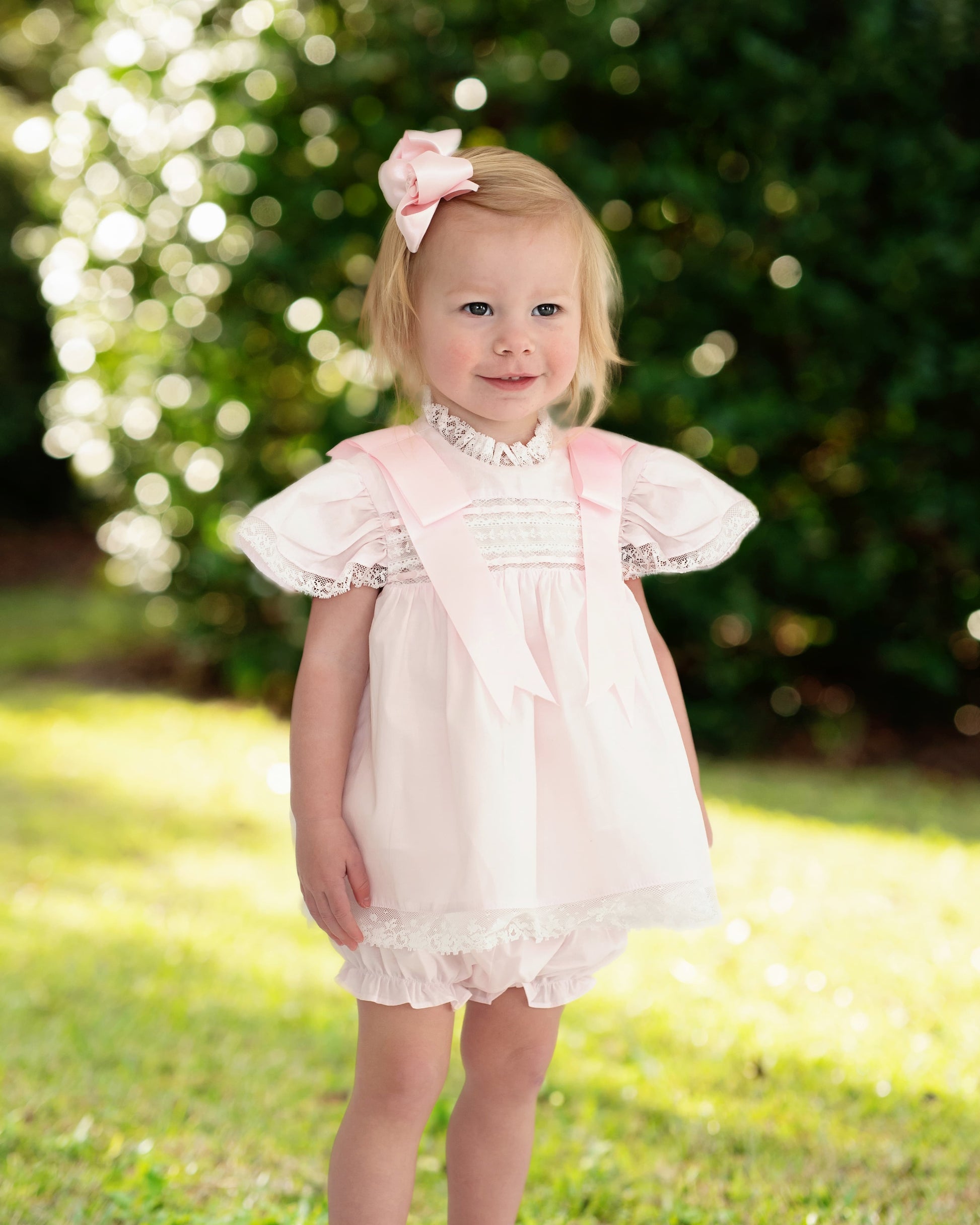 Young girl in a pink dress standing outdoors with a blurred green background