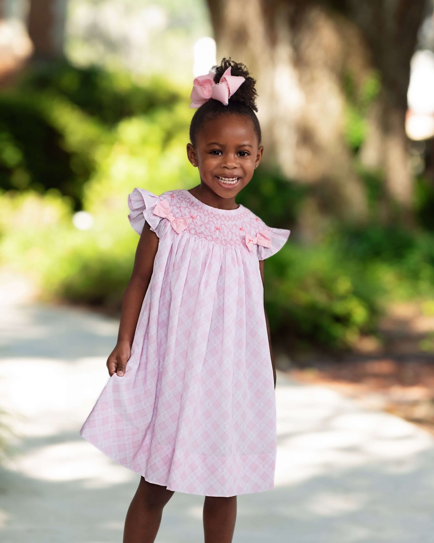 Young girl in a pink dress standing outdoors with greenery in the background