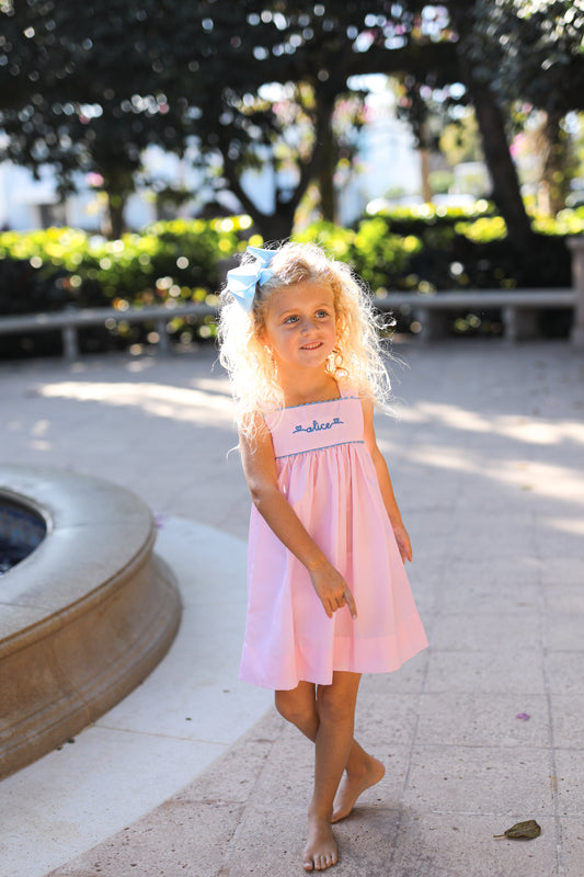 Young girl in a pink dress standing outdoors with greenery in the background