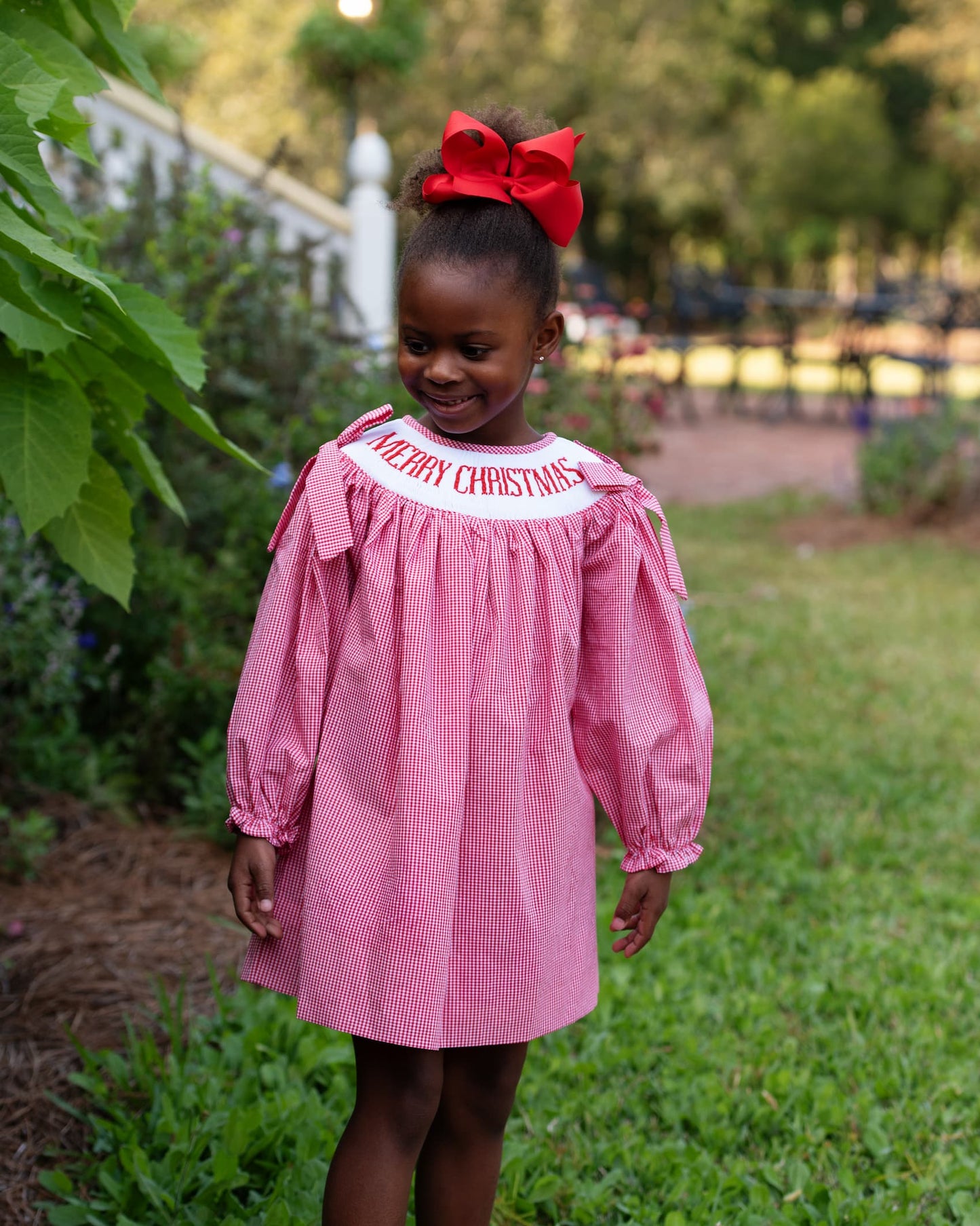 Young girl in a pink dress with 'Merry Christmas' on it, standing outdoors.