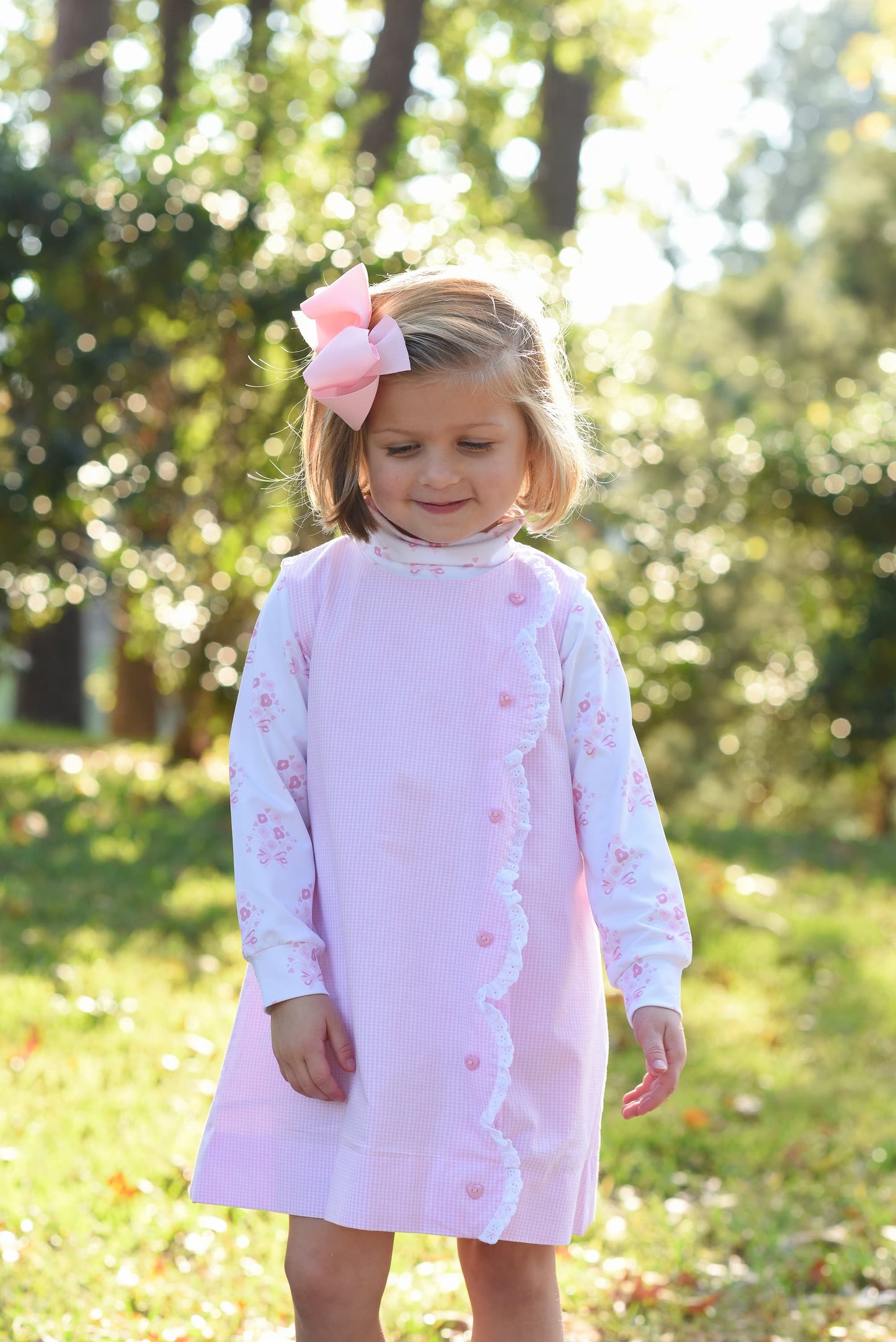 Young girl in a pink dress with a bow standing outdoors in a natural setting