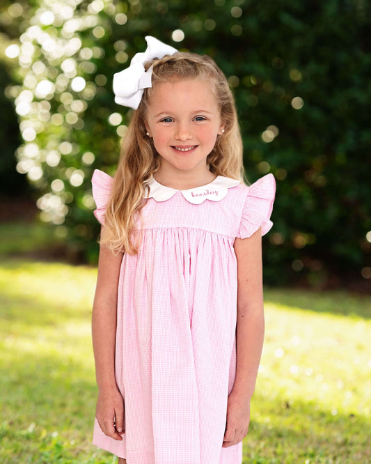 Young girl in a pink dress with a white bow in her hair, standing outdoors.