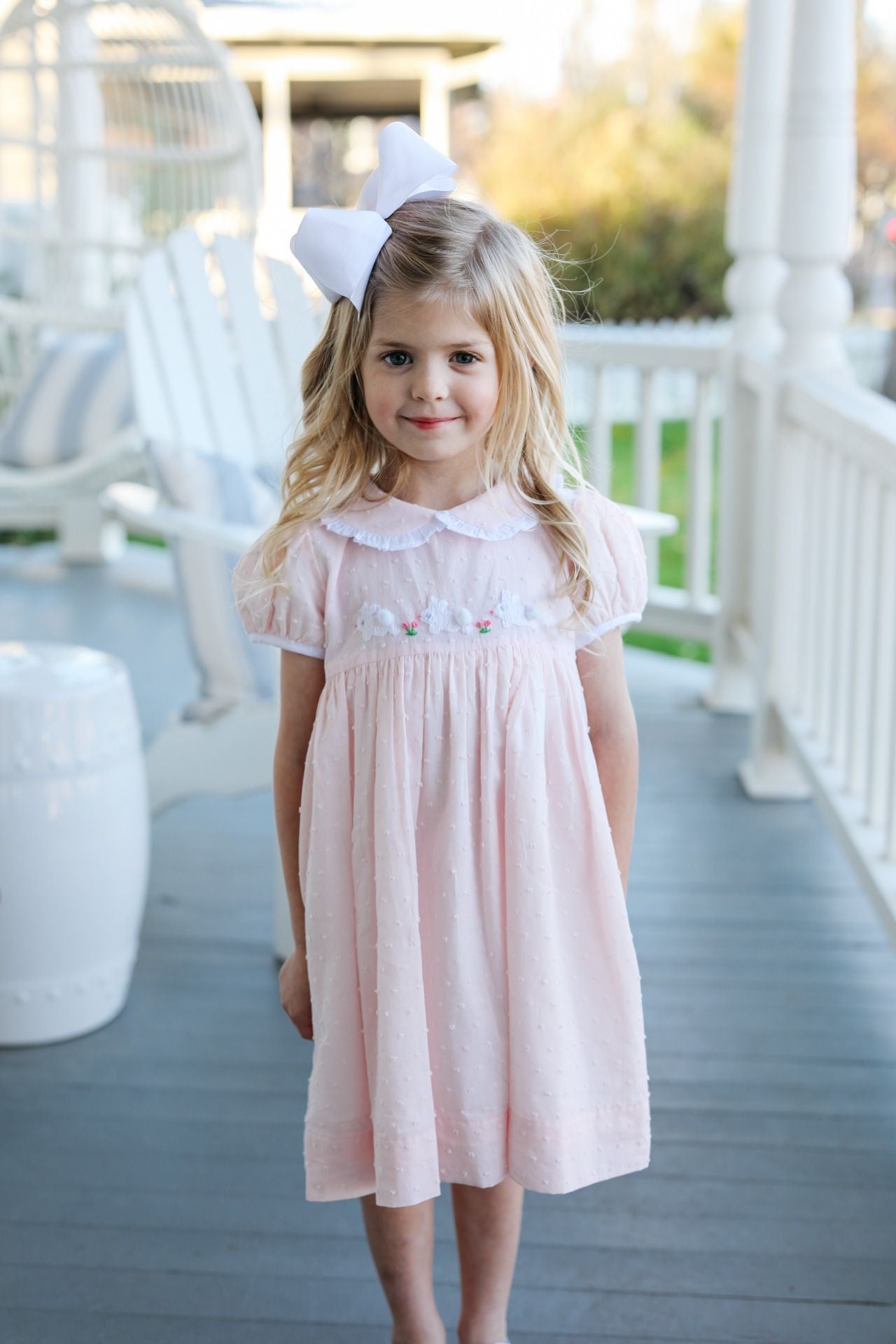 Young girl in a pink dress with a white bow on a porch