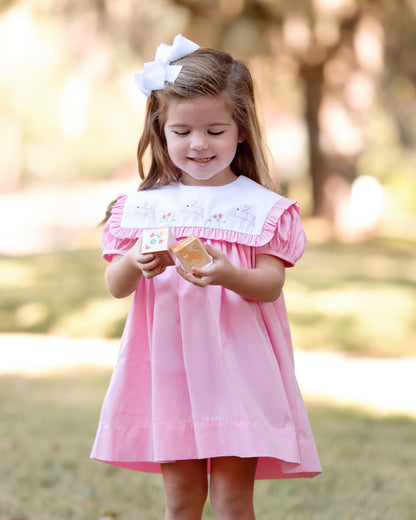 Young girl in a pink dress with a white bow standing outdoors.