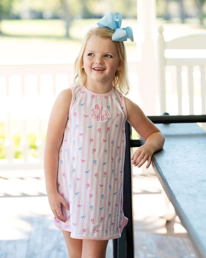 Young girl in a pink dress with floral patterns standing outdoors.