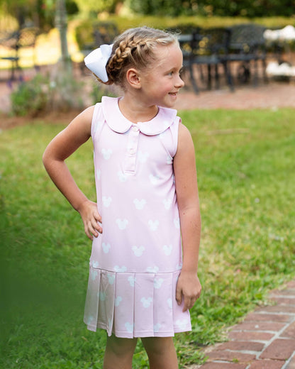 Young girl in a pink dress with heart patterns standing outdoors on a grassy area.