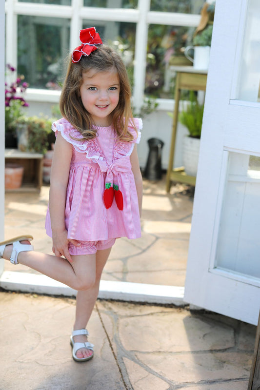 Young girl in a pink dress with red accents standing outdoors.