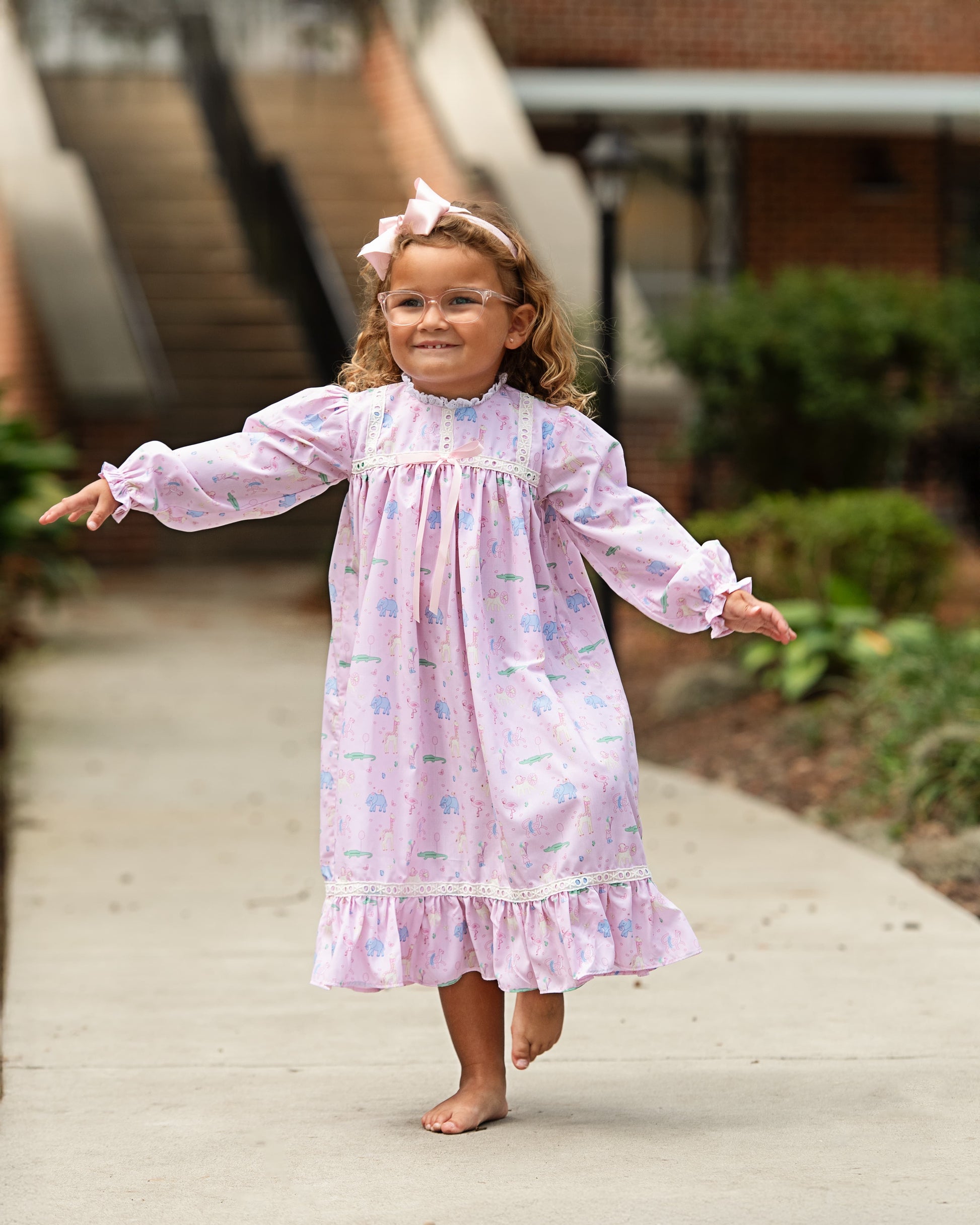 Young girl in a pink floral nightgown standing on a sidewalk with a blurred background
