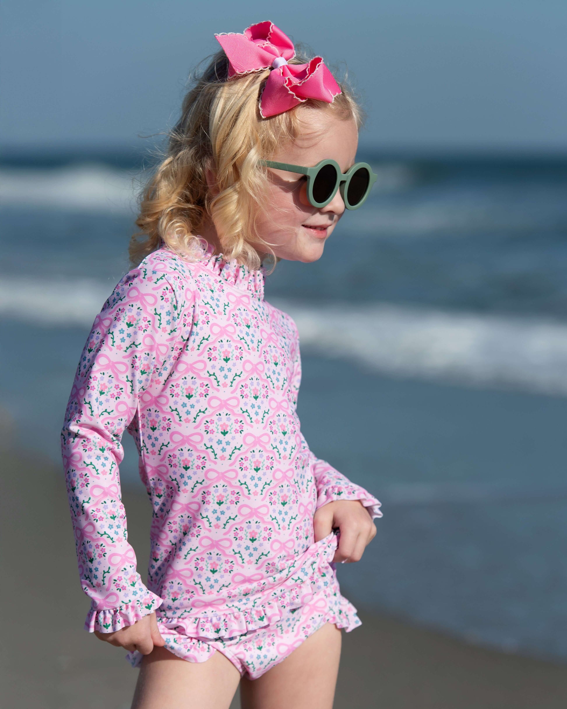 Young girl in a pink floral swimsuit and sunglasses on a beach