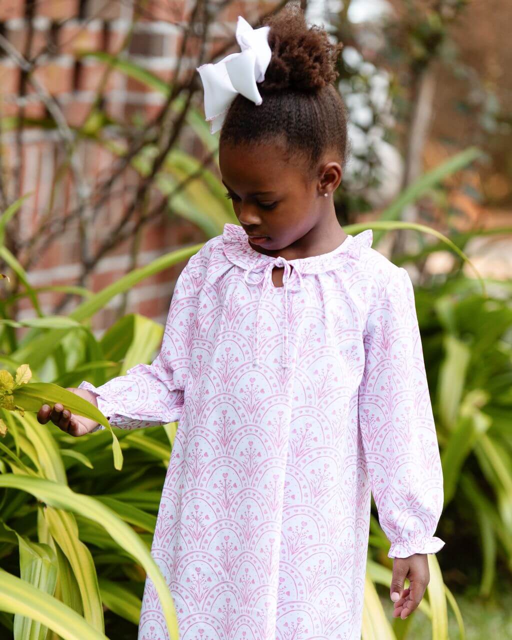 Young girl in a pink nightgown standing among green plants